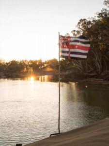 A flag overlooking the river. The flag has a Union Jack in the top left hand corner, blue and white stripes on the top and bottom and a red horizontal stripe in the middle as well as a vertical red stripe to the right of the Union Jack. There are stars on the flag as well.